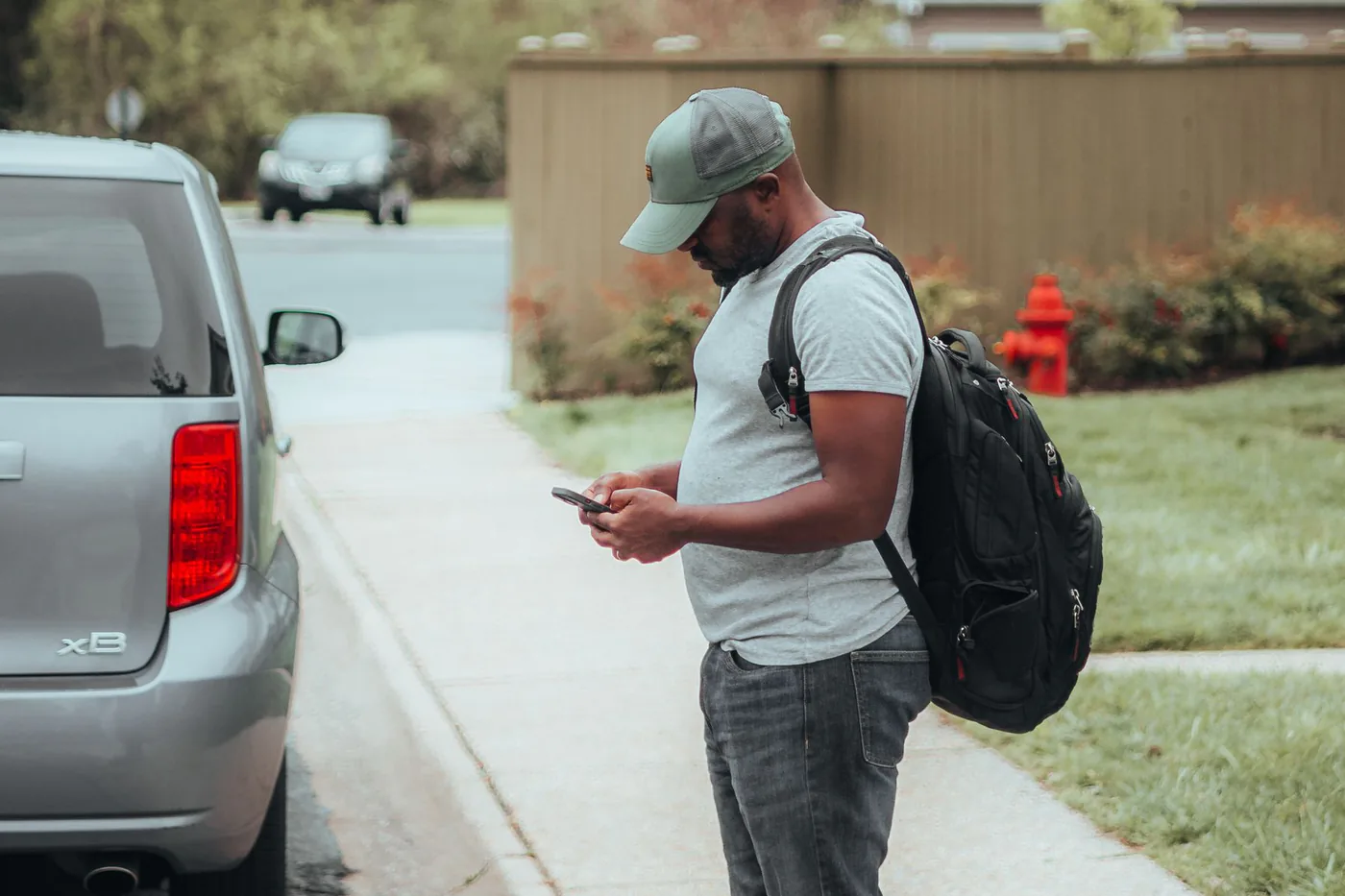 En bilejer står ved sin parkerede bil og ser på sin telefon