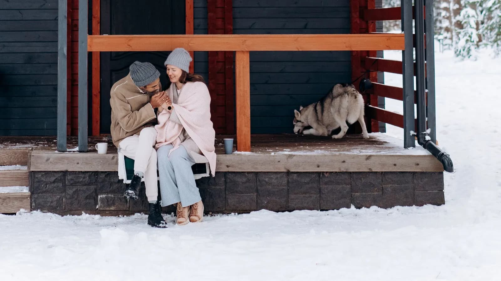 Par og hund ved et fritidshus i snevejr