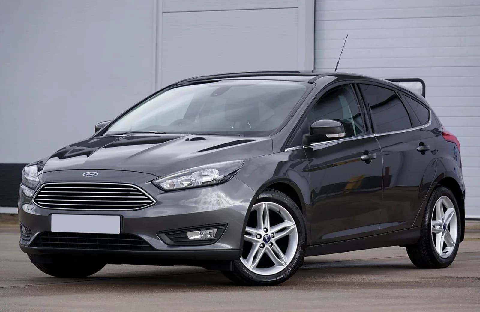 En grå Ford holder parkeret foran en garage