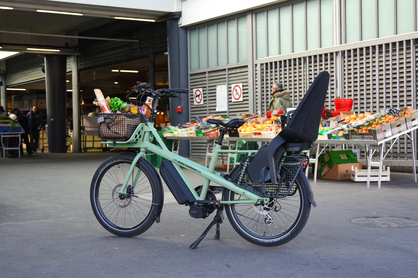 En elektrisk ladcykel med barnesæde og varer står ved et marked
